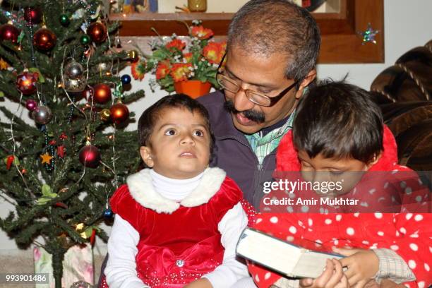 little sisters holding holy bible while sitting in their father lap on the eve of christmas 2017 - amir mukhtar stock pictures, royalty-free photos & images