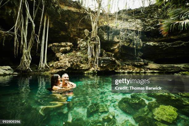 laughing couple embracing while swimming in cenote - hüfttief im wasser stock-fotos und bilder