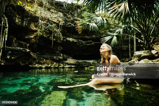 smiling girl sitting on edge of cenote after swim during family vacation - off the beaten path foto e immagini stock