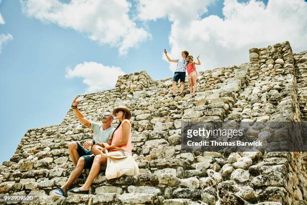family taking selfies with smartphones while exploring mayan ruins during vacation - 13 year old girls in shorts stock pictures, royalty-free photos & images
