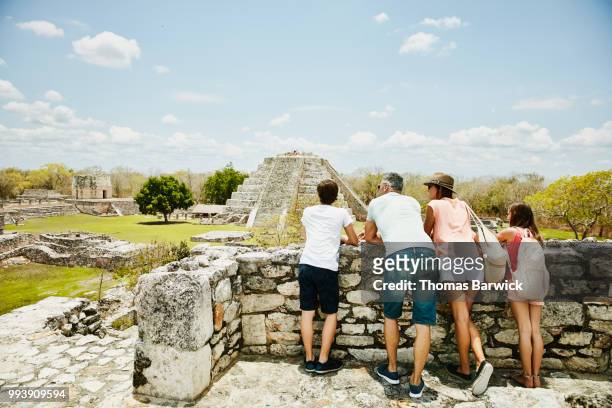 family looking at view while exploring mayapan ruins during vacation - groene korte broek stockfoto's en -beelden