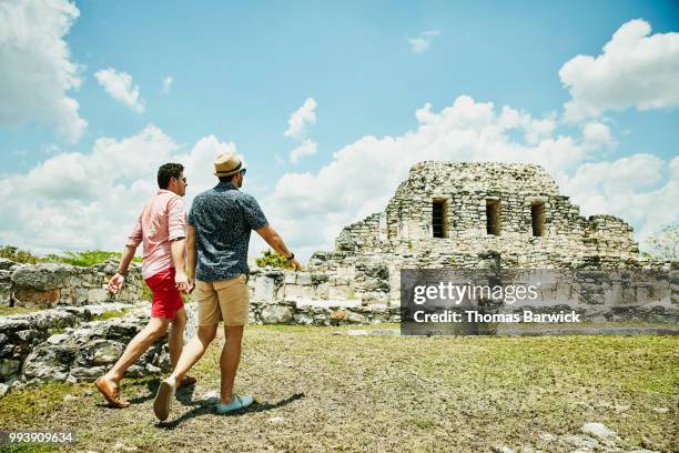 gay couple holding hands while exploring mayapan ruins during vacation - mayan stock pictures, royalty-free photos & images