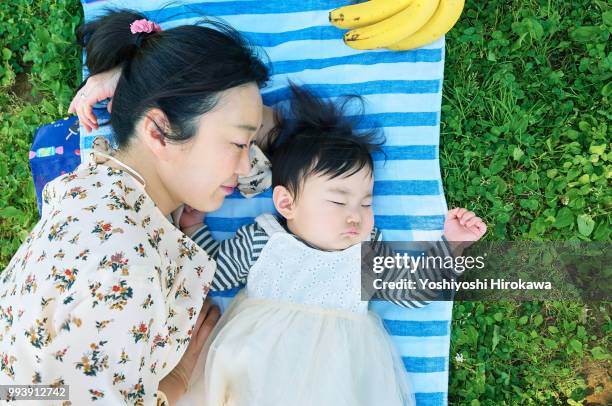 mother sleeping with toddler girl ( 6-11 months ) on lawn at park under sunshine - stadtteil koto stock-fotos und bilder