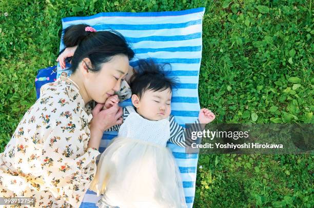 mother sleeping with toddler girl ( 6-11 months ) on lawn at park under sunshine - stadtteil koto stock-fotos und bilder