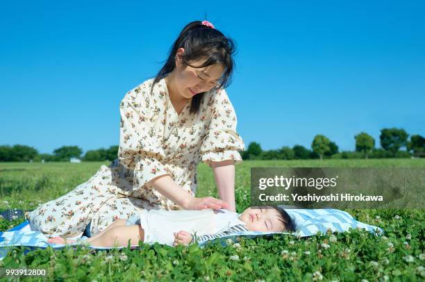 mother sleeping with toddler girl ( 6-11 months ) on lawn at park under sunshine - stadtteil koto stock-fotos und bilder