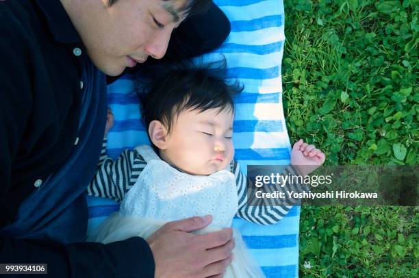 Father helping infant girl ( 6-11 months )  crawl at park under sunshine