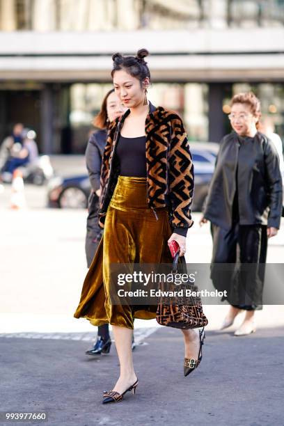 Guest wears a brown fluffy jacket with a printed Fendi logo, a balck top, a brown satin skirt, Fendi shoes, a Fendi brown bag , outside Fendi, during...