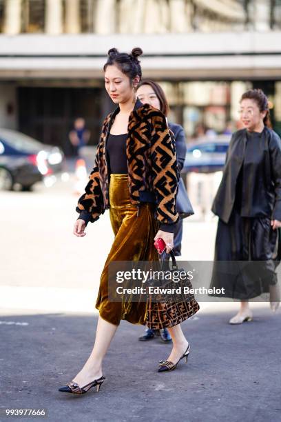 Guest wears a brown fluffy jacket with a printed Fendi logo, a balck top, a brown satin skirt, Fendi shoes, a Fendi brown bag , outside Fendi, during...