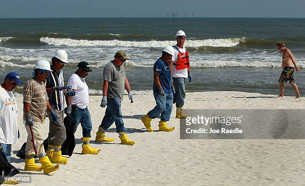 Workers search the beach for tar balls to be picked up as they wash ashore from the Deepwater Horizon site on May 14, 2010 in Dauphin Island,...