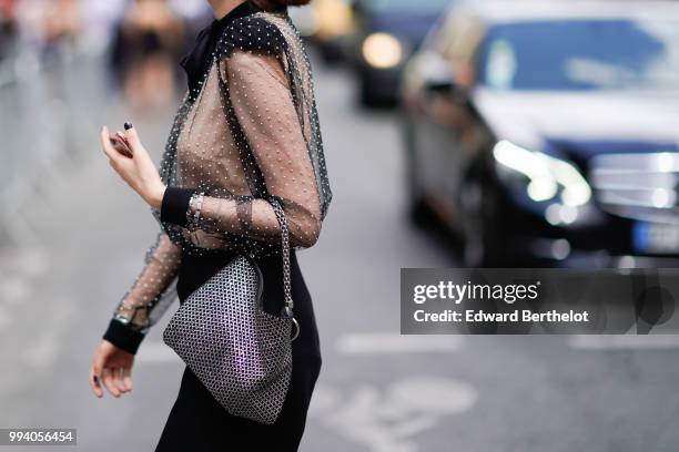 Guest wears a black lace mesh top, a black skirt, a bag with silver geometric patterns, earrings , outside Jean-Paul Gaultier, during Paris Fashion...