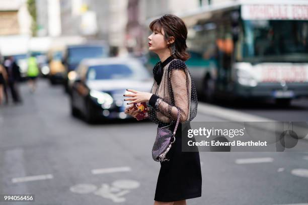 Guest wears a black lace mesh top, a black skirt, a bag with silver geometric patterns, earrings , outside Jean-Paul Gaultier, during Paris Fashion...