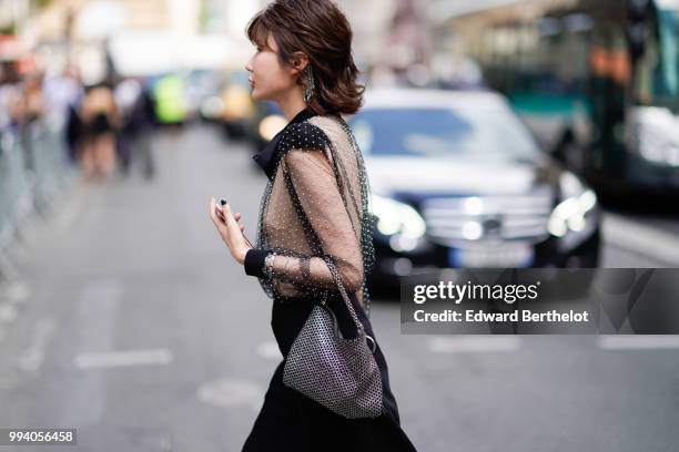 Guest wears a black lace mesh top, a black skirt, a bag with silver geometric patterns, earrings , outside Jean-Paul Gaultier, during Paris Fashion...