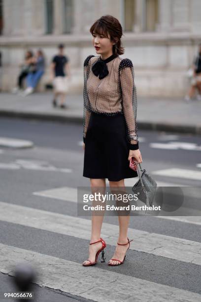 Guest wears a black lace mesh top, a black bow tie, a black skirt, red YSL Saint Laurent shoes with heels shaped as the YSL logo, a bag with silver...