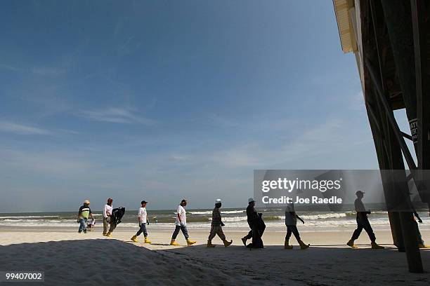 Workers search the beach for tar balls to be picked up as they wash ashore from the Deepwater Horizon site on May 14, 2010 in Dauphin Island,...