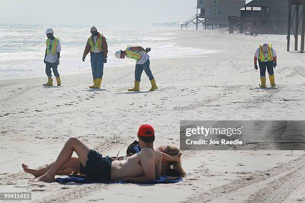 Workers search the beach for tar balls to be picked up as they wash ashore from the Deepwater Horizon site on May 14, 2010 in Dauphin Island,...