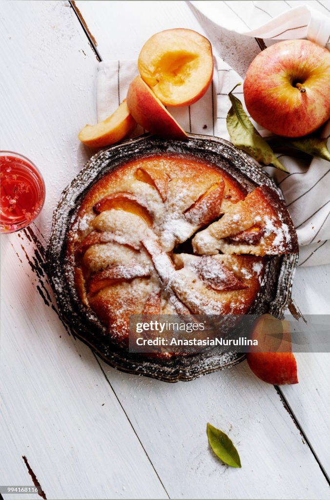 Sweet pie with fresh summer peaches on white wooden distressed background with a glass of rose water. Harvest time concept. Top view