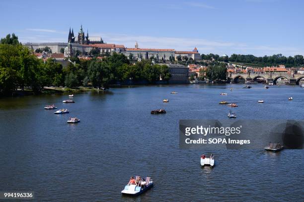 People navigating on small boats seen next to Prague Castle.
