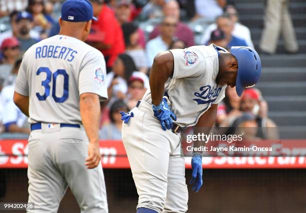 Manager Dave Roberts of the Los Angeles Dodgers checks on Yasiel Puig after he sustained a right intercostal oblique strain during his at bat in the...