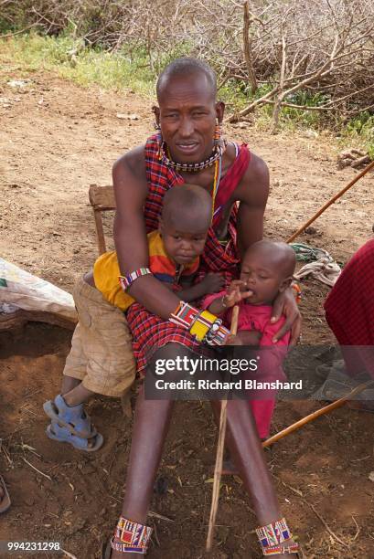 Maasai man sitting with two small children in Kenya, 2016.