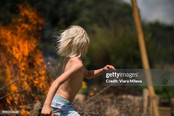 blond haired boy running away from garden bonfire - regarder par dessus son épaule photos et images de collection