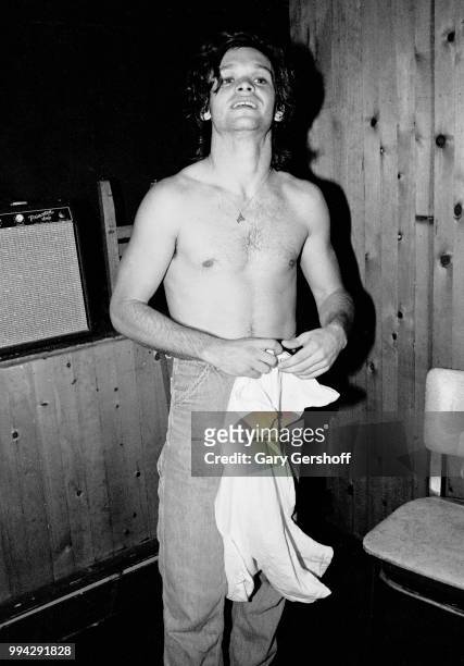 View of American Rock, County, and Folk musician John Cougar as he changes his shirt, backstage at the nightclub, My Father's Place, Roslyn, New...