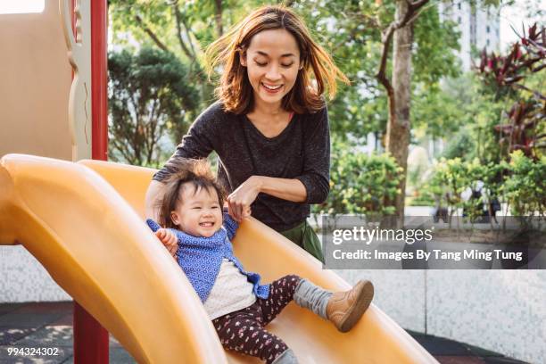 mom and lovely baby playing slide in playground joyfully. - área de juego fotografías e imágenes de stock