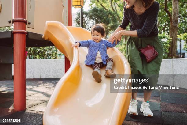 mom and lovely baby playing slide in playground joyfully. - playground equipment happy parent stock pictures, royalty-free photos & images