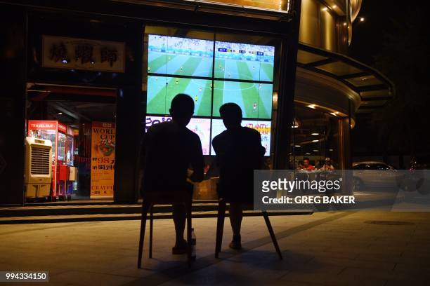 This photo taken on July 3, 2018 shows two football fans watching the 2018 Russia World Cup football match between Sweden and Switzerland on a TV...