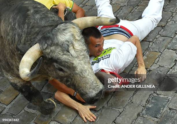 Participants fall next to a Cebada Gago fighting bull on the third day of the San Fermin bull run festival in Pamplona, northern Spain on July 9,...