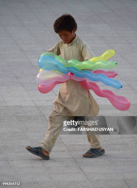In this photo taken on July 8, 2018 a young Afghan balloon vendor waits for customers in the courtyard of Hazrat-e-Ali shrine or Blue Mosque, in...