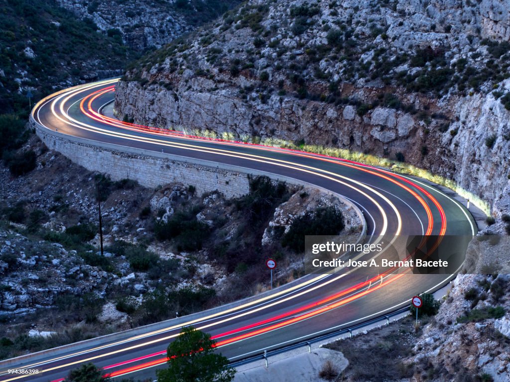 Lights and trails of vehicles, cars and trucks, circulating along a road of mountain between ravines with circular curves closed in the night.