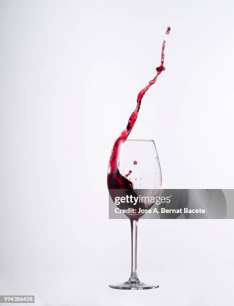 red wine splashing in glass in front of white background - kurzzeitfotografie stock-fotos und bilder