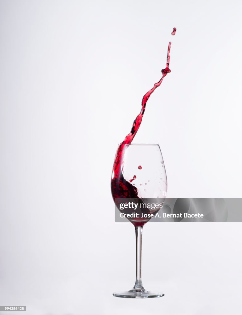 Red wine splashing in glass in front of white background