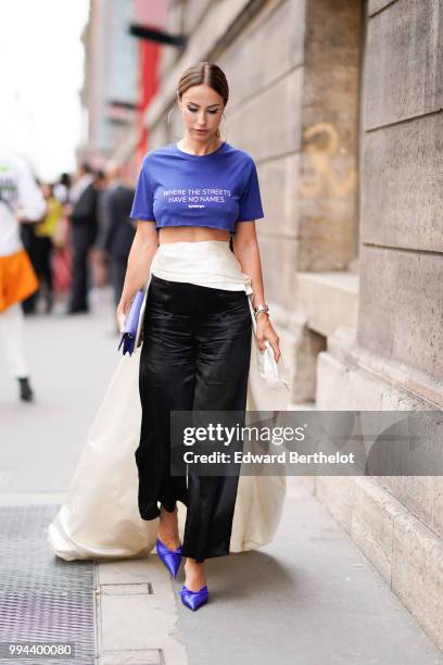 Guest wears a blue cropped bare belly t-shirt with the printed sentence "where the streets have no names", a white skirt, black flared pants, blue...
