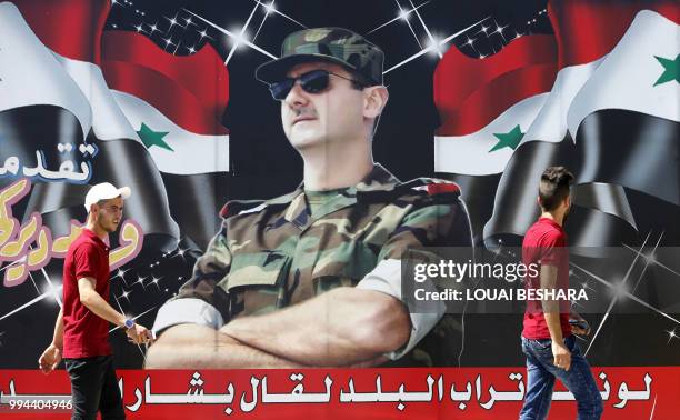 Syrian youths walk past a billboard showing a picture of Syrian President Bashar al-Assad wearing sunglasses while dressed in a Field Marshal's...