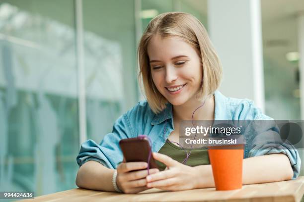 una giovane donna attraente di 20 anni con un telefono cellulare e cuffie che ascoltano la musica - 20 24 years photos foto e immagini stock