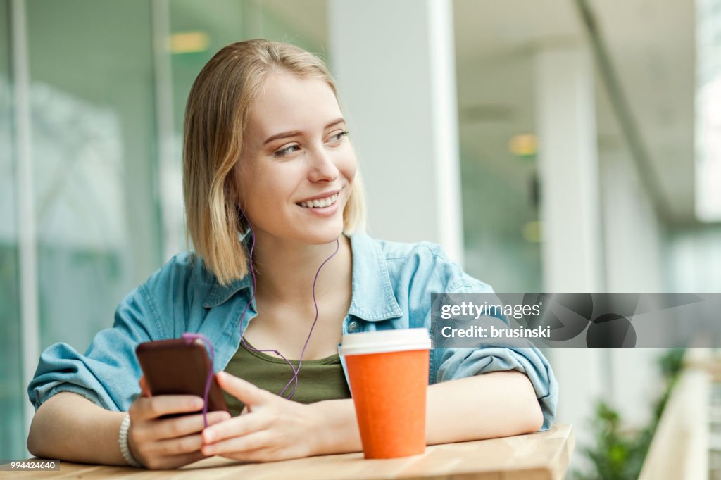 A young attractive woman of 20 years with a mobile phone and headphones listening to music