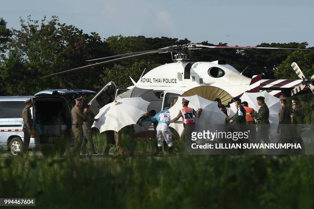 Police and military personnel use umbrellas to cover around a stretcher near a helicopter and an ambulance at a military airport in Chiang Rai on...