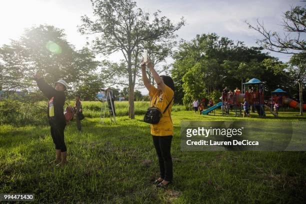 Onlookers watch and cheer as a helicopter flies towards an airstrip near Tham Luang Nang Non cave to transport the fifth boy rescued from the cave to...