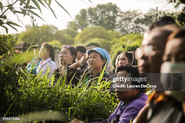 Onlookers watch and cheer as a helicopter flies towards an airstrip near Tham Luang Nang Non cave to transport the fifth boy rescued from the cave to...