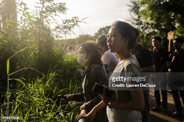 Onlookers watch and cheer as a helicopter flies towards an airstrip near Tham Luang Nang Non cave to transport the fifth boy rescued from the cave to...