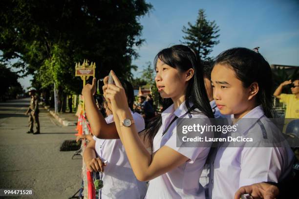 Onlookers watch and cheer as a helicopter flies towards an airstrip near Tham Luang Nang Non cave to transport the fifth boy rescued from the cave to...