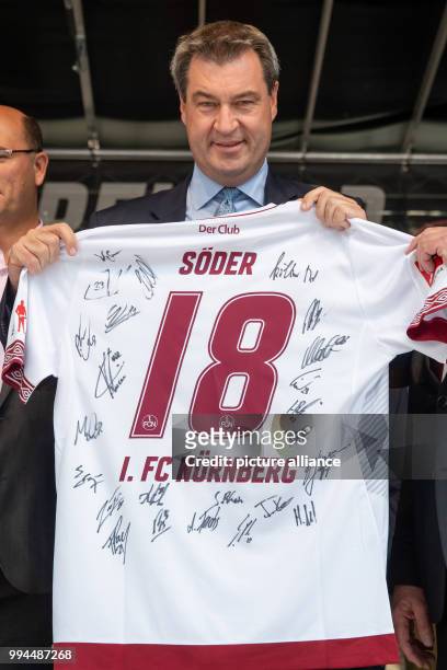July 2018, Germany, Nuremberg: Markus Soeder of the Christian Social Union , Premier of Bavaria, holds up a shirt with his name and the autographs of...