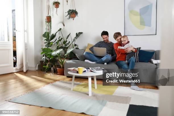 family sitting on couch, using laptop - family livingroom stock-fotos und bilder