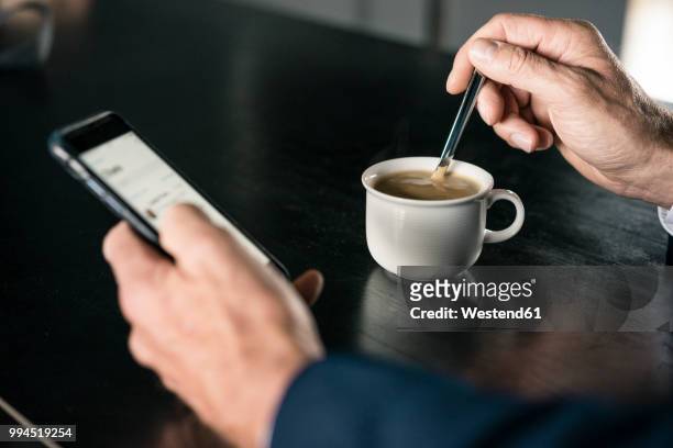 close-up of businessman with cup of coffee using cell phone - spoon in hand stock-fotos und bilder