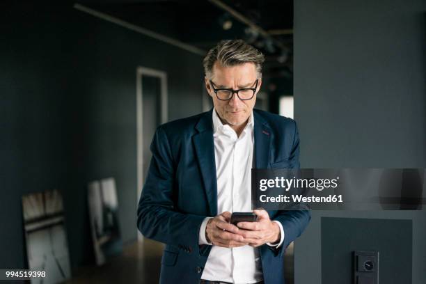 mature businessman standing in office using cell phone - business texting stock pictures, royalty-free photos & images