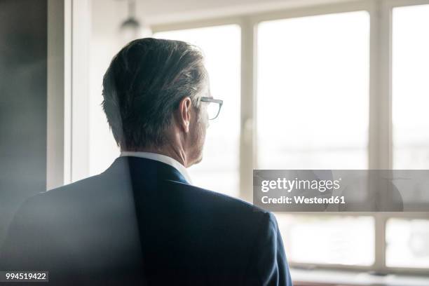 rear view of mature businessman looking out of window - ビジネスフォーマル ストックフォトと画像