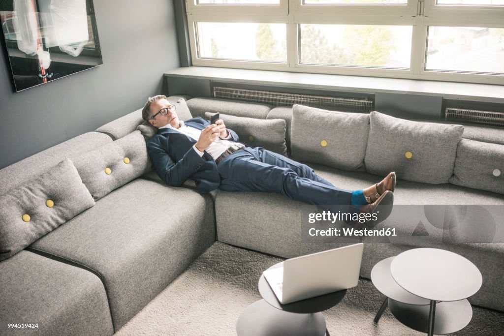 Mature businessman lying on couch using cell phone