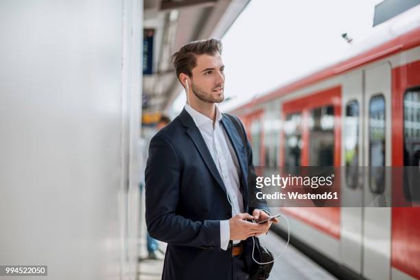 businessman at the station with earbuds and cell phone - passagierzug stock-fotos und bilder