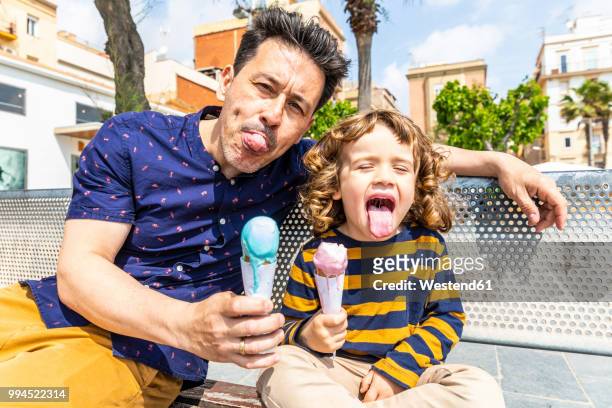 spain, barcelona, happy father and son sitting on bench enjoying an ice cream - funny face stock pictures, royalty-free photos & images